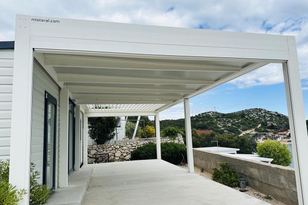Bela fiksna pergola, ki se popolnoma prilega sodobnemu zunanjemu prostoru in zagotavlja zaščito pred soncem in dežjem.